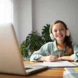 girl learning on laptop Smiling girl wearing headphones writing on a notebook with a laptop in front on the table