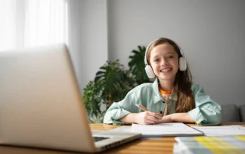 girl learning on laptop Smiling girl wearing headphones writing on a notebook with a laptop in front on the table